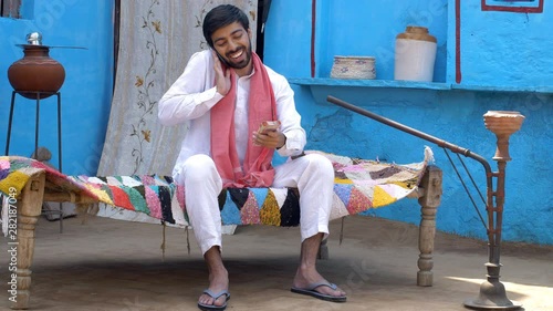 Attractive Indian villager taking a phone-call about receiving money - financial concept. Young happy farmer confirming on a phone call about receiving his hardworking income / salary to her mother...
