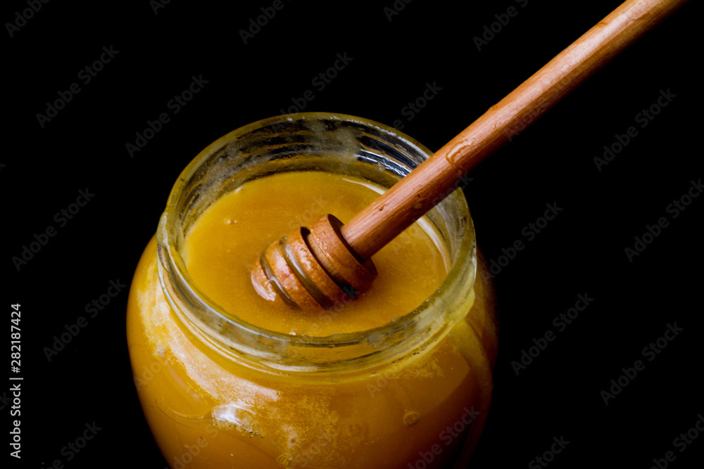 yellow, sweet honey in a glass jar with a wooden spoon. delicious, sticky honey on a black background. food. Copy space. Breakfast. vitamins. vegetarianism. healthy and healthy food. yellow, sweet honey in a glass jar with a wooden spoon. delicious, sticky honey on a black background. food. Copy space. Breakfast. vitamins. vegetarianism. healthy and healthy food.
