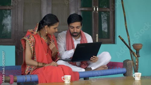 Young educated villager teaching basic usage of computer to his wife - village lifestyle. Beautiful Indian wife learning usage of computer from her husband while sitting on a charpai - relationship... photo
