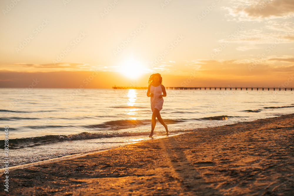 silhouette of young slim beautiful woman on sunset beach. Girl is running in a white dress. Late summer concept silhouette of young slim beautiful woman on sunset beach. Girl is running in a white dress. Late summer concept