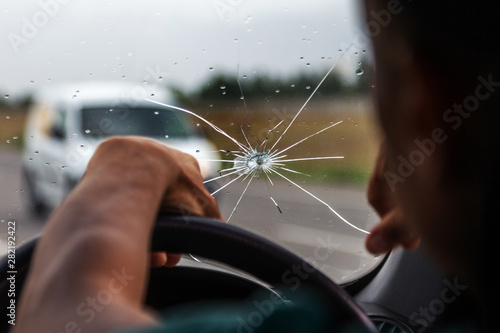 Broken windshield of a car. A web of radial splits, cracks on the triplex windshield. Broken car windshield, damaged glass with traces of oncoming stone on road or from bullet trace in car glass photo