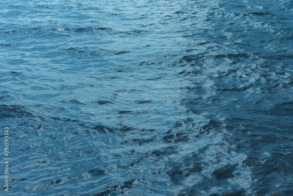 Obraz premium Blue water with waves and sun reflections background