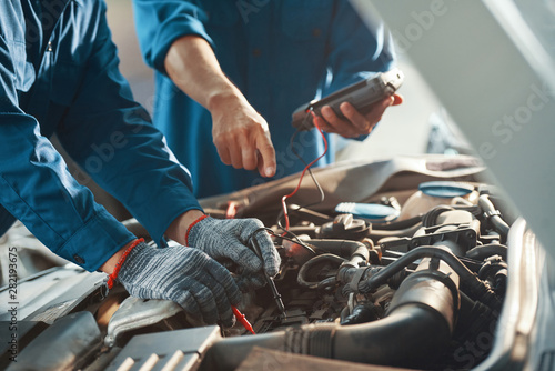 Close-up image of professional mechanics testing car battery with multimeter