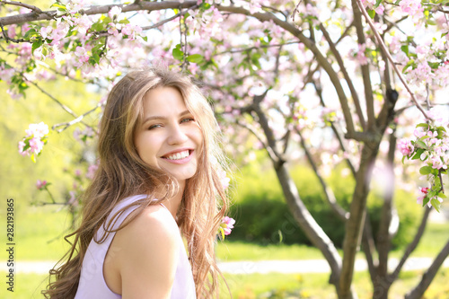 Beautiful young woman near blooming tree on spring day