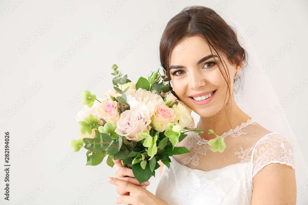 Naklejka premium Beautiful young bride with bouquet of flowers on light background