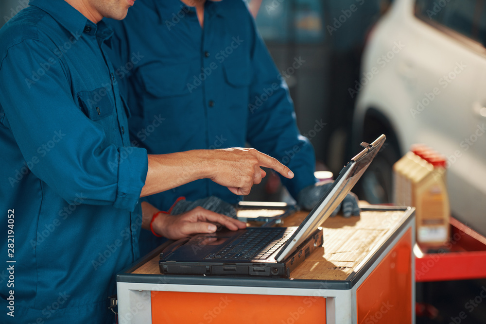 Cropped image of mechanic pointing at laptop screen and discussing results of car computer diagnostics with coworker