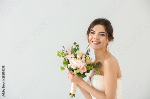 Beautiful young bride with bouquet of flowers on light background