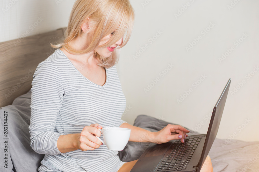 Naklejka premium Pretty woman using laptop while having a cup of coffee on bed
