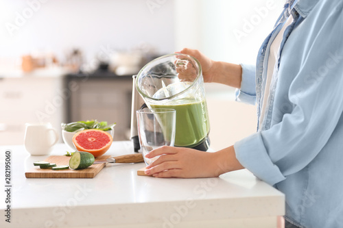 Woman pouring tasty smoothie from blender into glass in kitchen