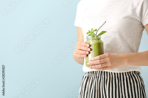 Young woman with tasty smoothie in mason jar on color background, closeup