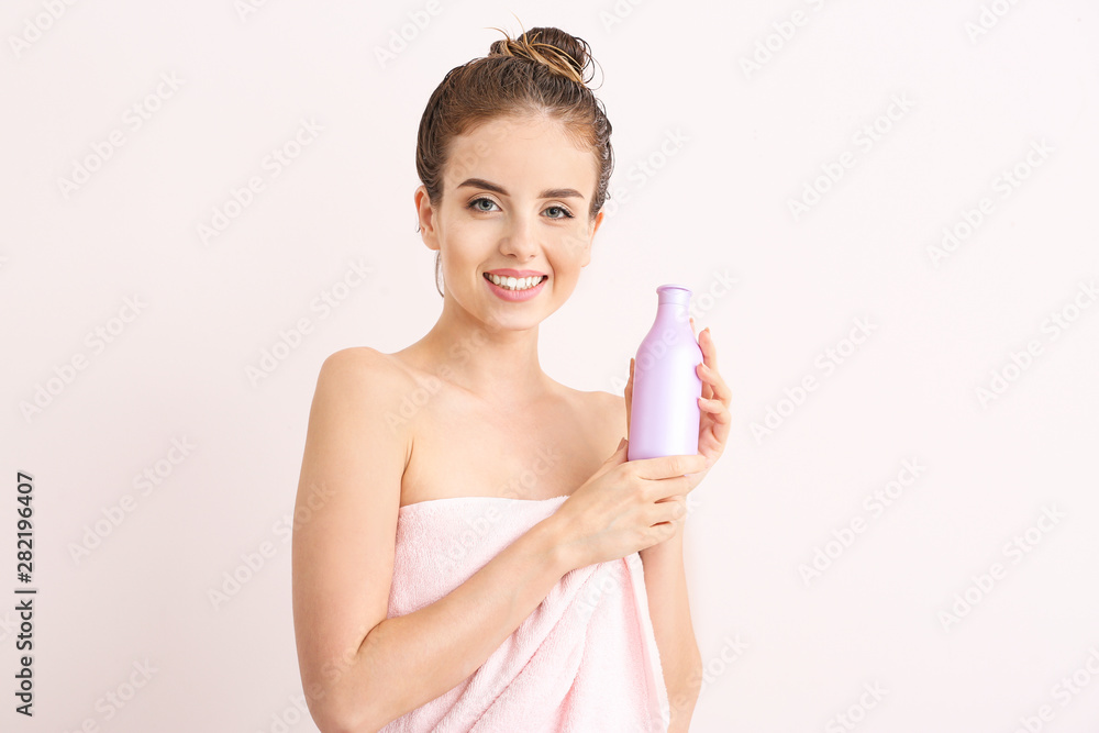Beautiful young woman with bottle of shampoo against light color background Beautiful young woman with bottle of shampoo against light color background