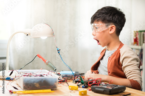 Smart looking preteen / teenage Asian boy wowing with mouth open wide successfully repairing, solid state relay in laboratory, wearing protective / safety glasses. Electronics, Sciences school project photo