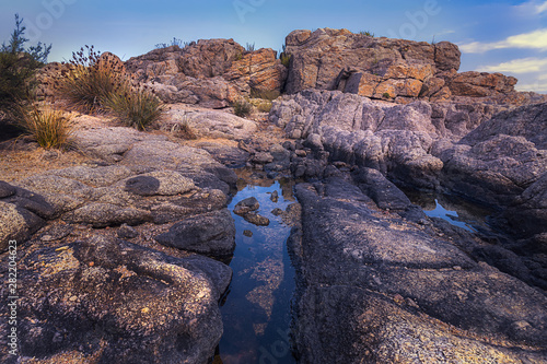 Beautiful rose colored stones, some vegetation & clear blue sky scene in a mediterranean rocky coast at Playa de Aro, Spain