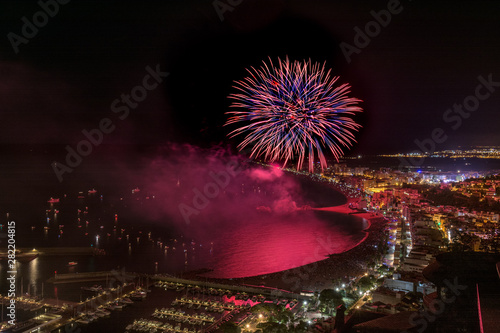 Awesome fireworks above the Blanes in Catalonia, Spain lighting the coast waters beside the enlightened city into a deep magenta