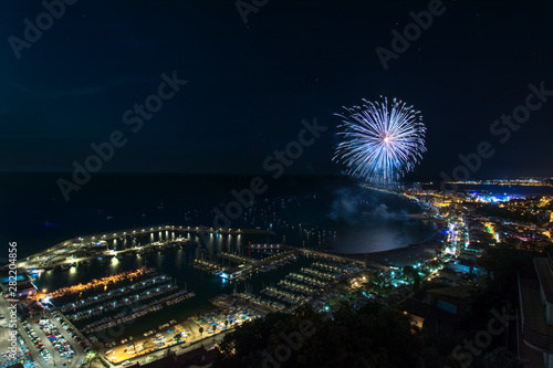 Awesome wide angle shot of fireworks above the Blanes in Catalonia, Spain lighting the coast waters beside the enlightened city & dock