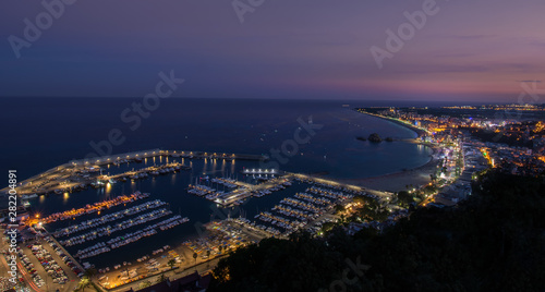 Blue hour at the mediterranean coast of Blanes in Catalonia, Spain. Slightly blue-reddish sky & beautifuly enlightened dock & city