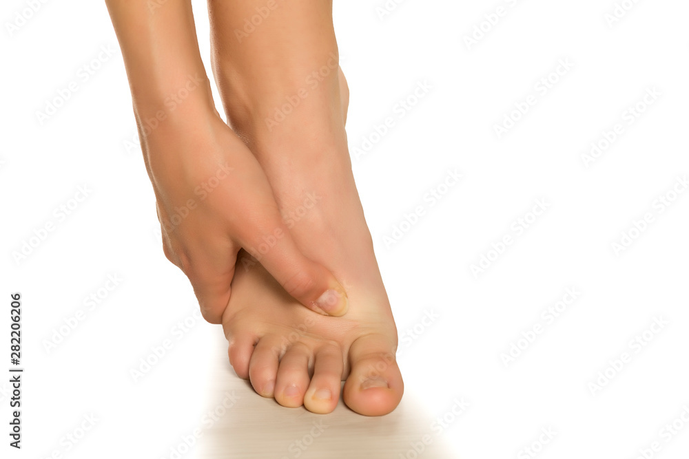 Young woman's beautiful bare foot, pointing with her finger to a foot point. Closeup Isolated on white background.