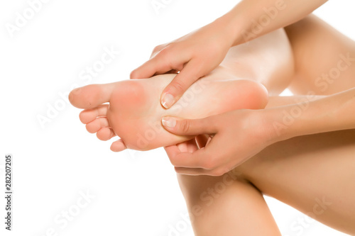 Young woman massaging her tired painful feet. Closeup isolated on white background.
