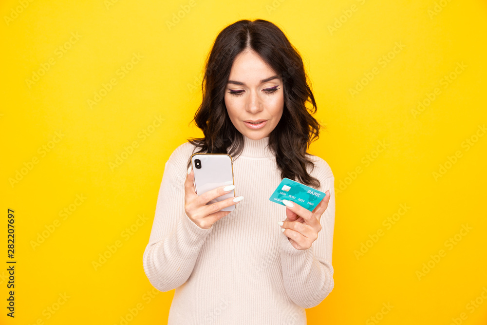 Woman using phone and credit card isolated at the yellow background Woman using phone and credit card isolated at the yellow background