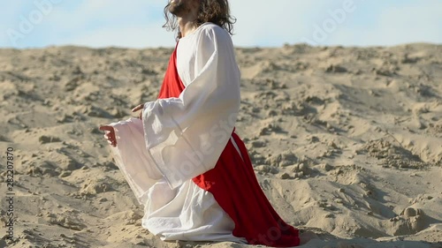 Smiling Jesus in desert falling on knees, raising hands to heaven, praying God photo