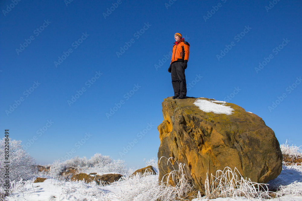 winter man on the rock,on a large rock stands a young man in winter and looks at the beauty of a winter morning