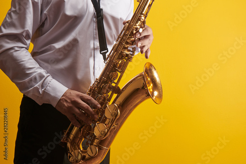Portrait of professional musician saxophonist man in white shirt plays jazz music on saxophone, yellow background in a photo studio, side view