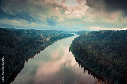 Landscape from the height of the river under a cloudy sky with wooded banks