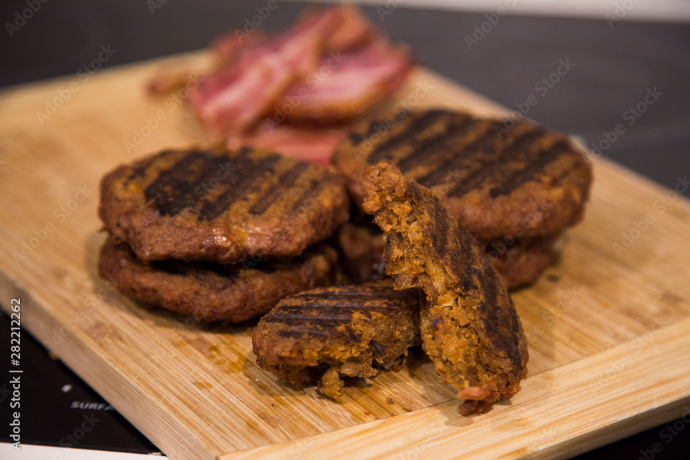 Vegan burger patties sitting on a wooden board with bacon. When eating