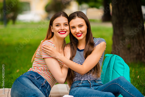 Portrait of sweet girls with red lips-stick cuddling wearing striped t-shirt denim jeans sitting on plaid blanket in town