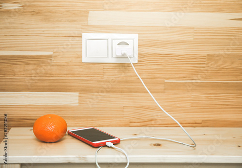 Smartphone and orange are lying on the bedside table. Stylish minimalist photo. Mobile is charging.