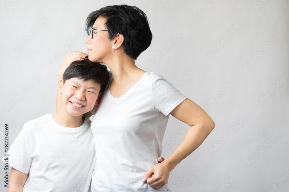 A smart and beautiful asian mom holding her preteen son with love. Her son leans his head on her chest smiling happily. Love expression, Parenting teen, Single mom, Young son, Mommy's love Concept. - obrazy, fototapety, plakaty 