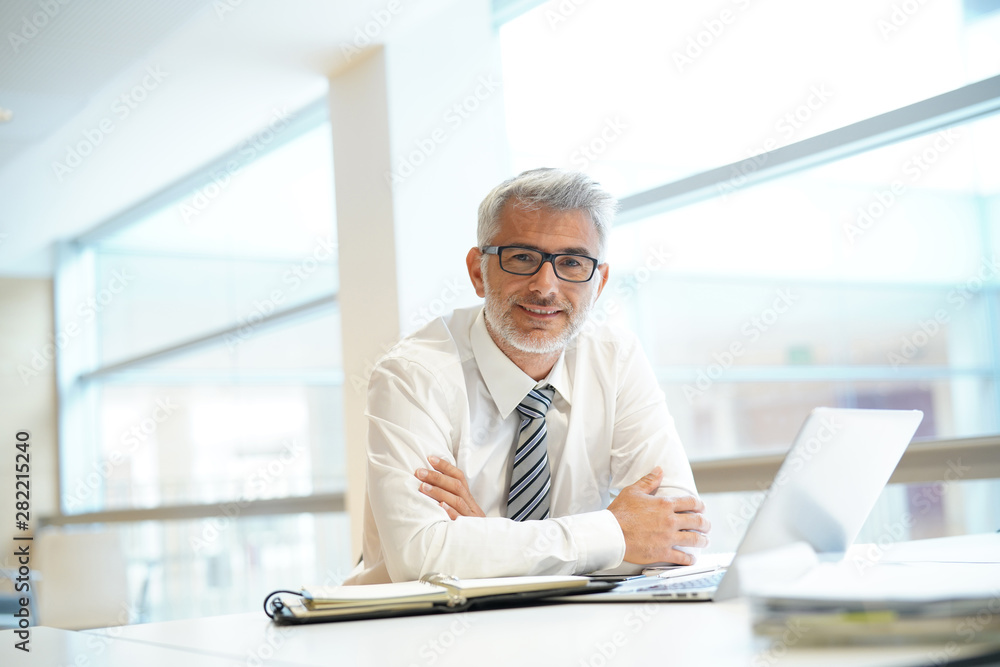 Portrait of smiling businessman sitting at desk in contemporary office Portrait of smiling businessman sitting at desk in contemporary office
