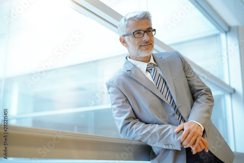 Mature businessman leaning on window in modern office photo