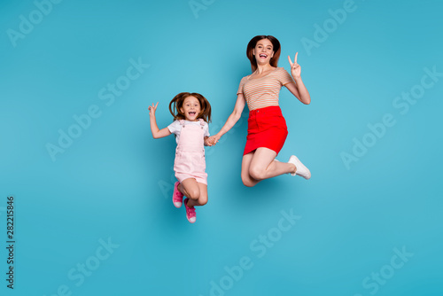 Full body photo of foxy little lady and mom showing v-sign symbols jumping high wear casual clothes isolated blue background