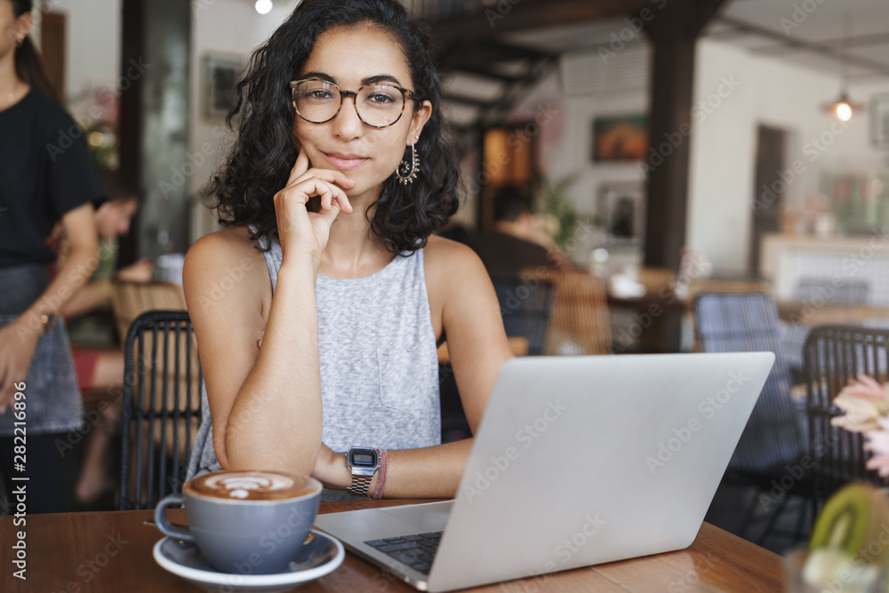 Freelance, e-learning and business concept. Attractive stylish hipster girl, female student prepare university project sit alone coffee table, co-working space, drink cappuccino, working with laptop Freelance, e-learning and business concept. Attractive stylish hipster girl, female student prepare university project sit alone coffee table, co-working space, drink cappuccino, working with laptop