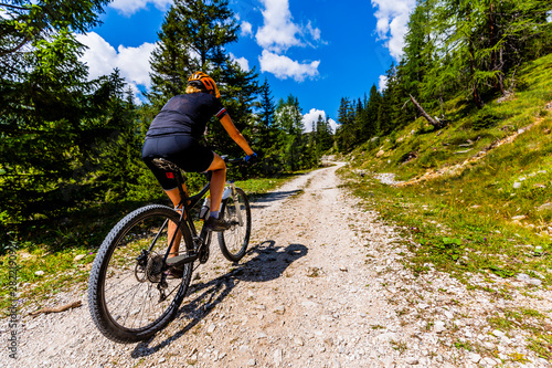Tourist cycling in Cortina d'Ampezzo, stunning rocky mountains on the background. Woman riding MTB enduro flow trail. South Tyrol province of Italy, Dolomites.