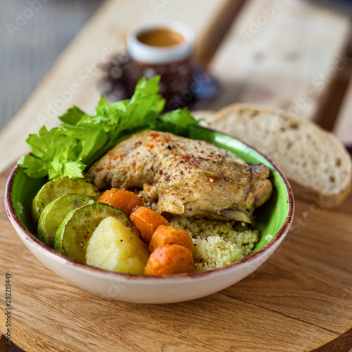Boiled chicken leg and potatoes with zucchini, carrots and herbs served with bread and coffee on a wooden background