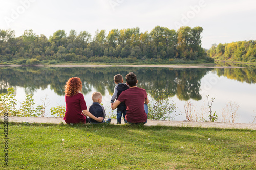Parenthood, nature, people concept - family with two sons sitting near the lake