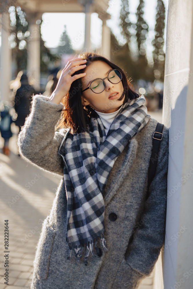 Attractive young girl wearing glasses in a coat walking on a sunny day