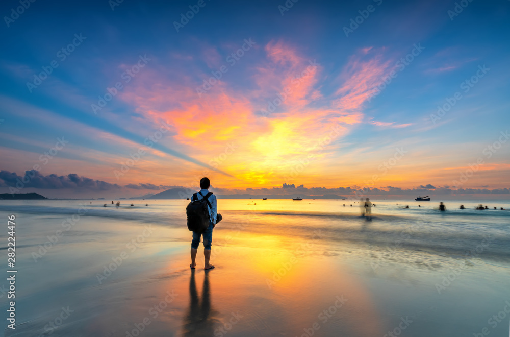 Silhouette of man backpacker on the beach looking at magical dramatic sunrise. The man standing on the sandy beach
