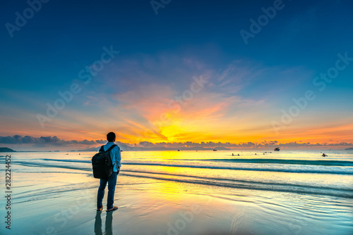Silhouette of man backpacker on the beach looking at magical dramatic sunrise. The man standing on the sandy beach
