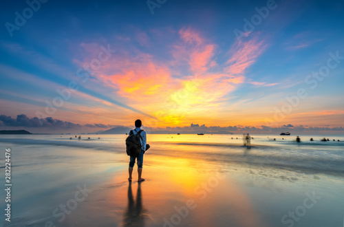 Silhouette of man backpacker on the beach looking at magical dramatic sunrise. The man standing on the sandy beach © huythoai