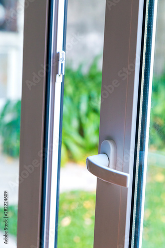 Open door of a family home. Close-up of the lock on the sliding door with the yard of background. White PVC door and double glass.