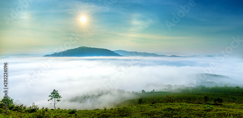 Dawn on a mountain plateau Da Lat, Vietnam beneath mist covered valleys and the sun rising over sky filled yellow color. 