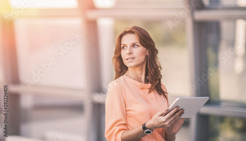 successful business woman with digital tablet standing near a large window in a modern office