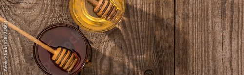panoramic shot of jars with honey and honey dippers on wooden table in sunlight