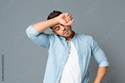 Exhausted hispanic man wiping sweat off forehead on gray background