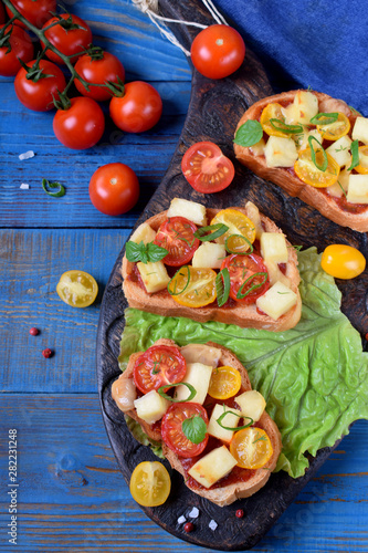 Fototapeta Naklejka Na Ścianę i Meble -  Bruschetta with different sorts of cherry tomatoes and soft cheese on the dark wood board on the blue table