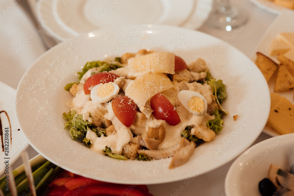 Caesar salad with croutons, quail eggs, cherry tomatoes and chicken in white plate on celebrate table Caesar salad with croutons, quail eggs, cherry tomatoes and chicken in white plate on celebrate table