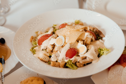 Caesar salad with croutons, quail eggs, cherry tomatoes and  chicken in white plate on celebrate table